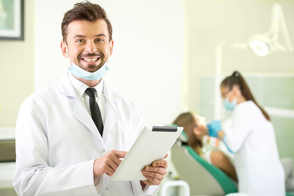 Smiling,Dentist,With,A,Tablet,In,Hands.,Another,Dentist,And